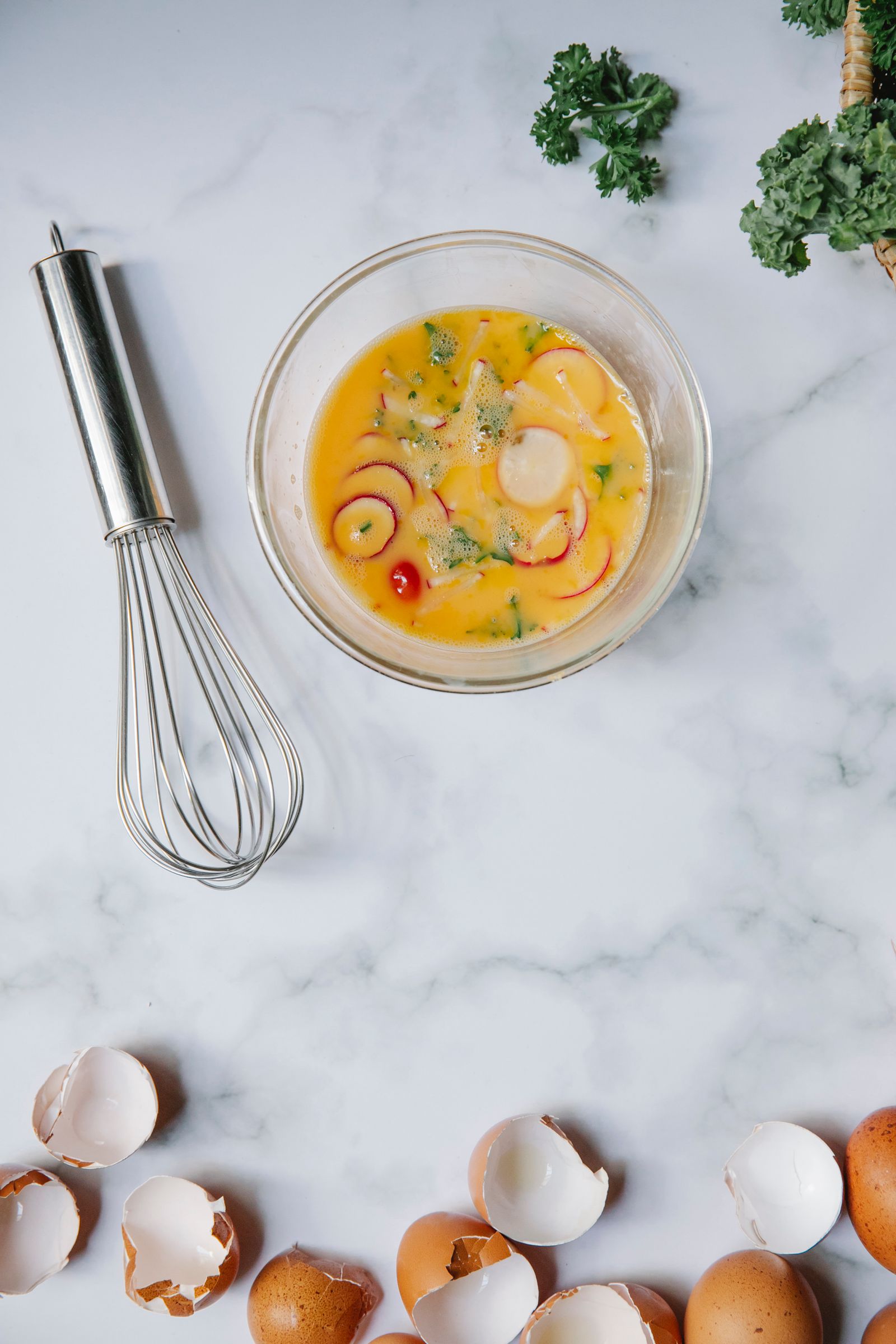 Whisked eggs in a glass bowl beside a whisk and eggshells on a marble counter