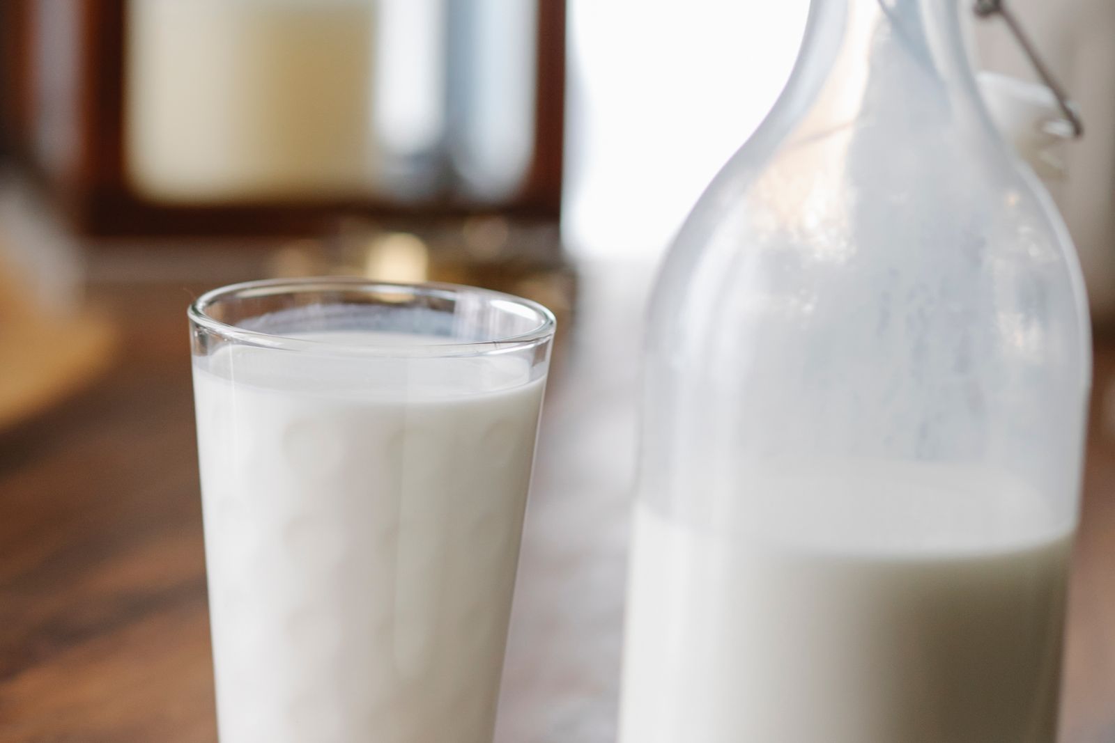 A full glass of kefir standing beside a glass bottle of the same fermented milk drink on a wooden table
