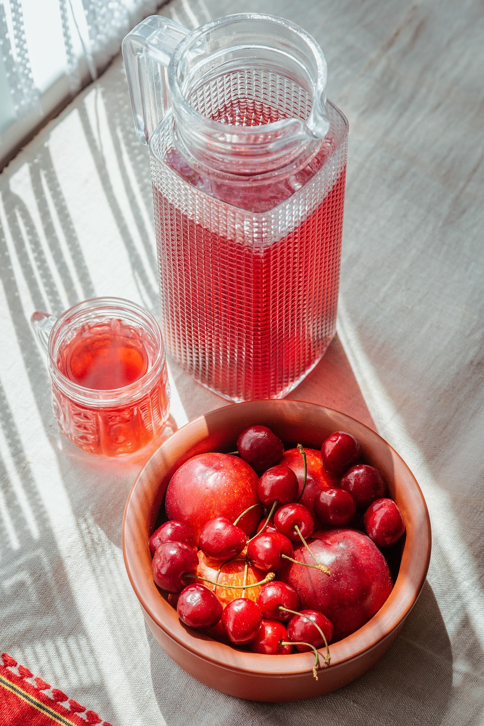 A pitcher and glass of deep red cherry juice beside a bowl of fresh cherries