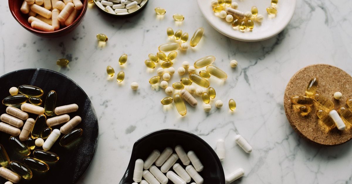 Bowls of supplement capsules and softgels on a marble surface