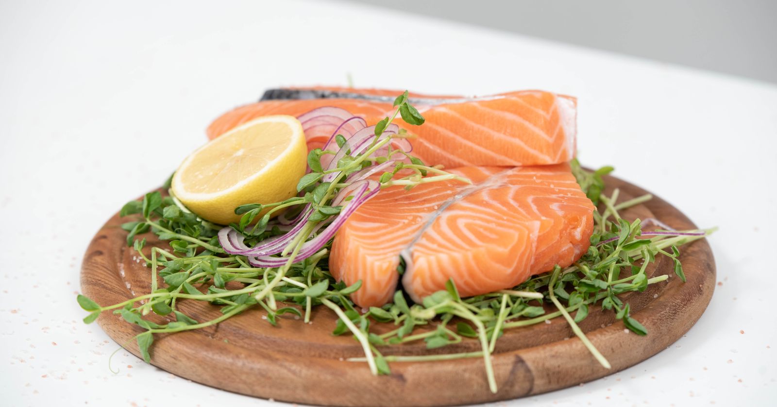 Fresh salmon fillets with lemon and greens on a wood board