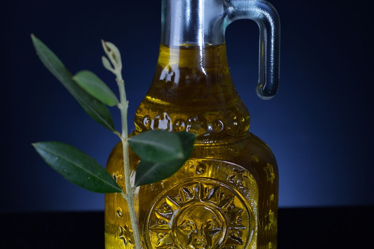 A glass cruet of golden extra virgin olive oil with an olive branch