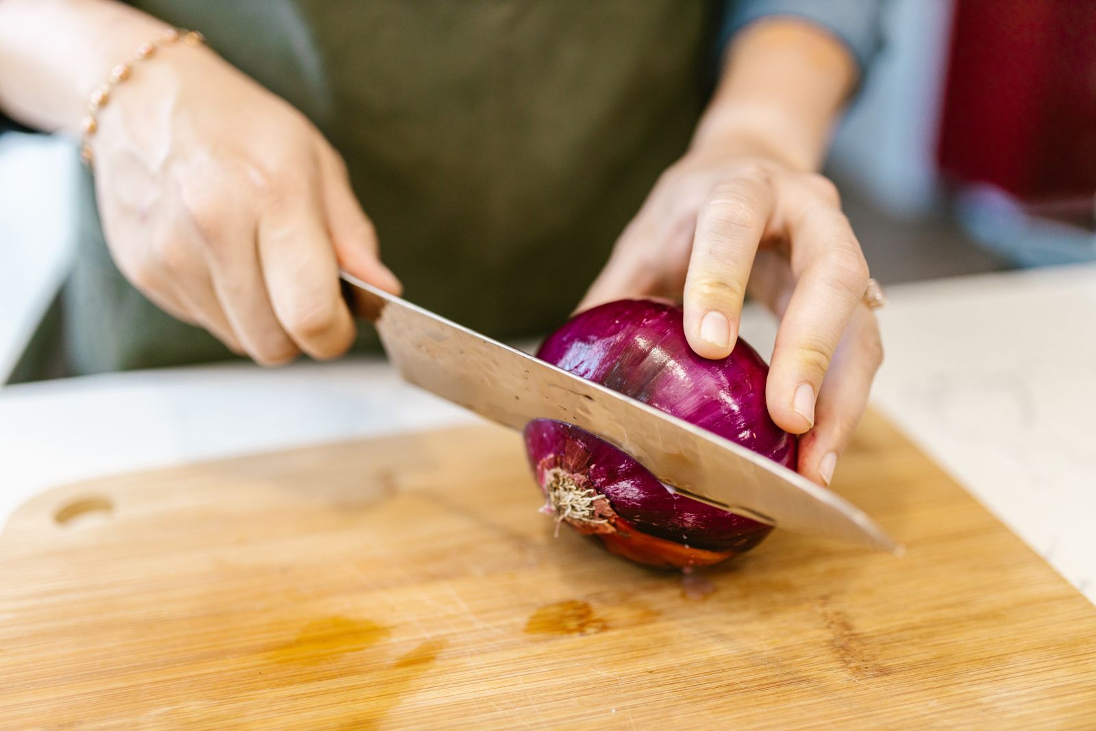 Hands slicing a red onion on a wooden board