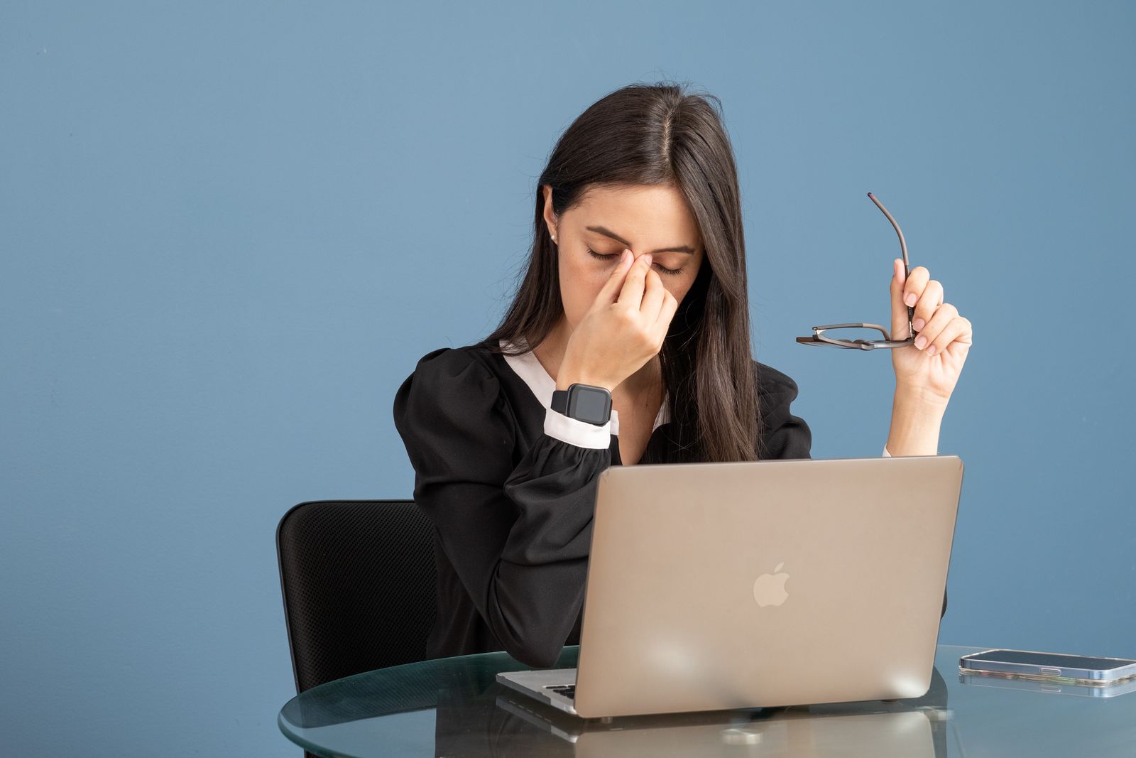 A person at a desk pressing the bridge of their nose in front of a laptop