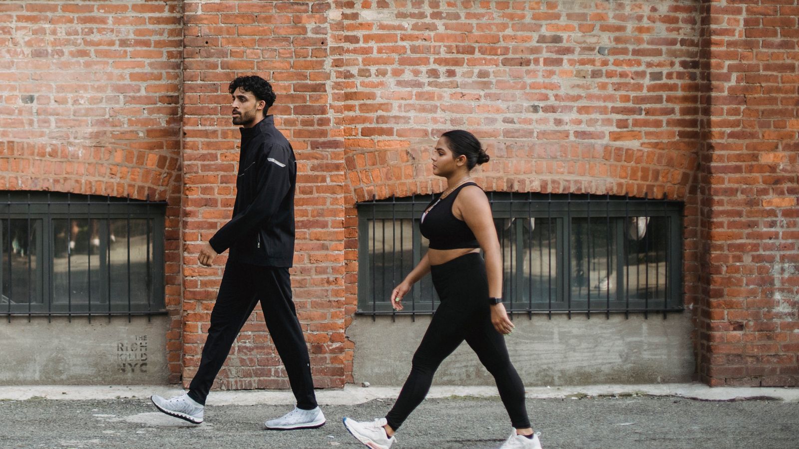 Two adults walking briskly side by side along a brick wall