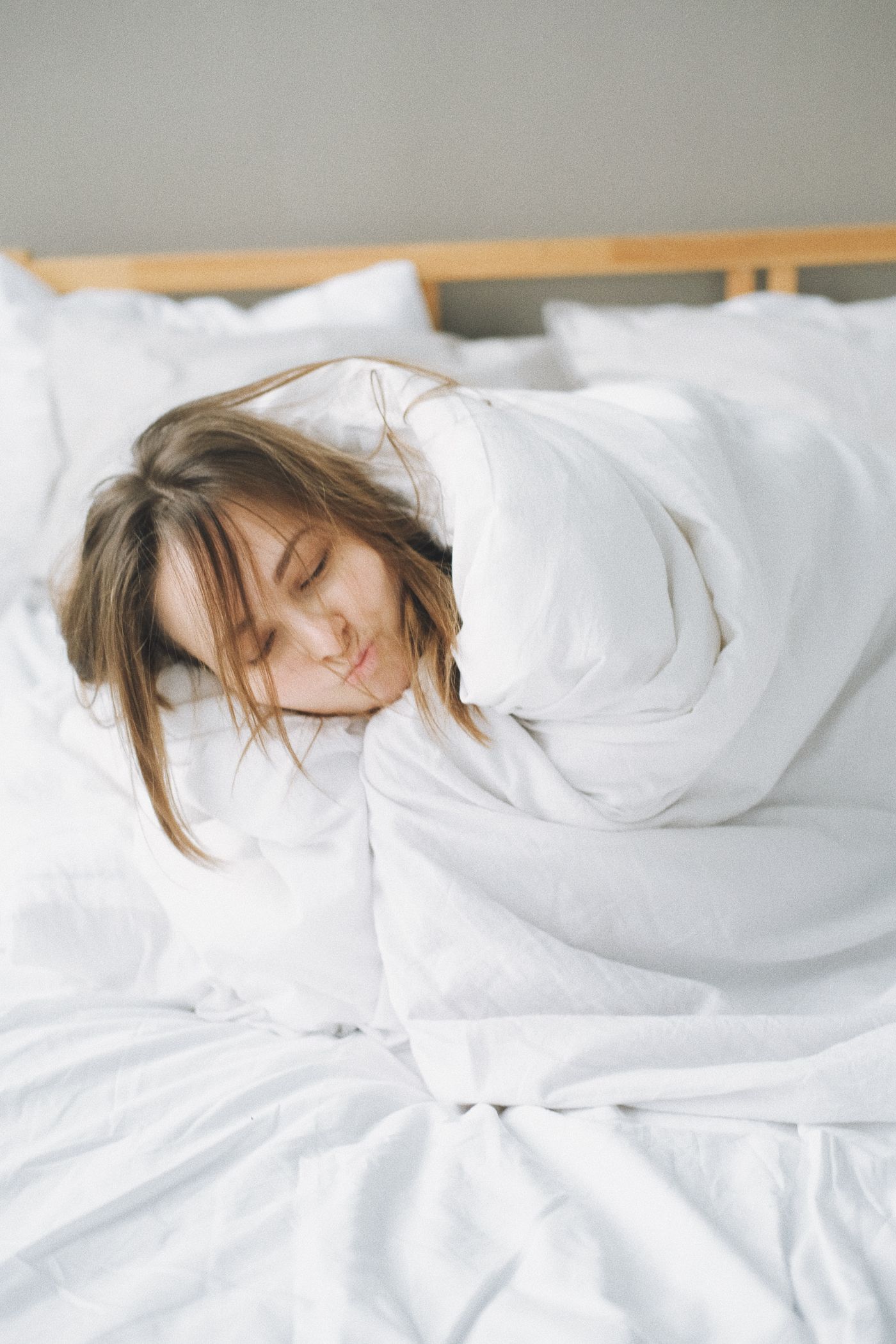 A woman asleep, wrapped in white bedding in soft morning light
