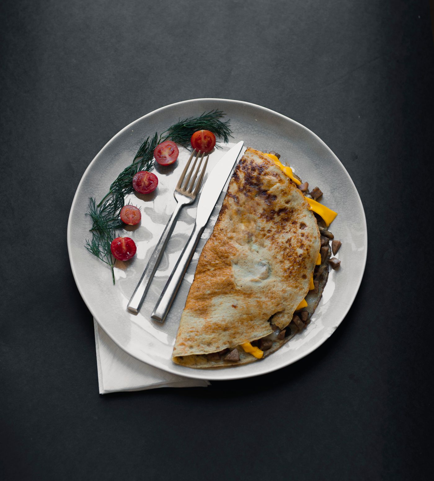A cheese and meat omelette on a plate with a fork and knife