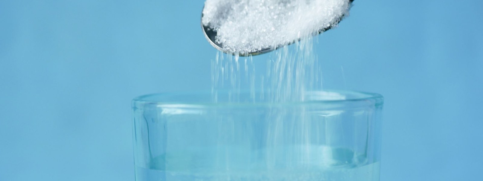 White powder being poured from a spoon into a glass of water