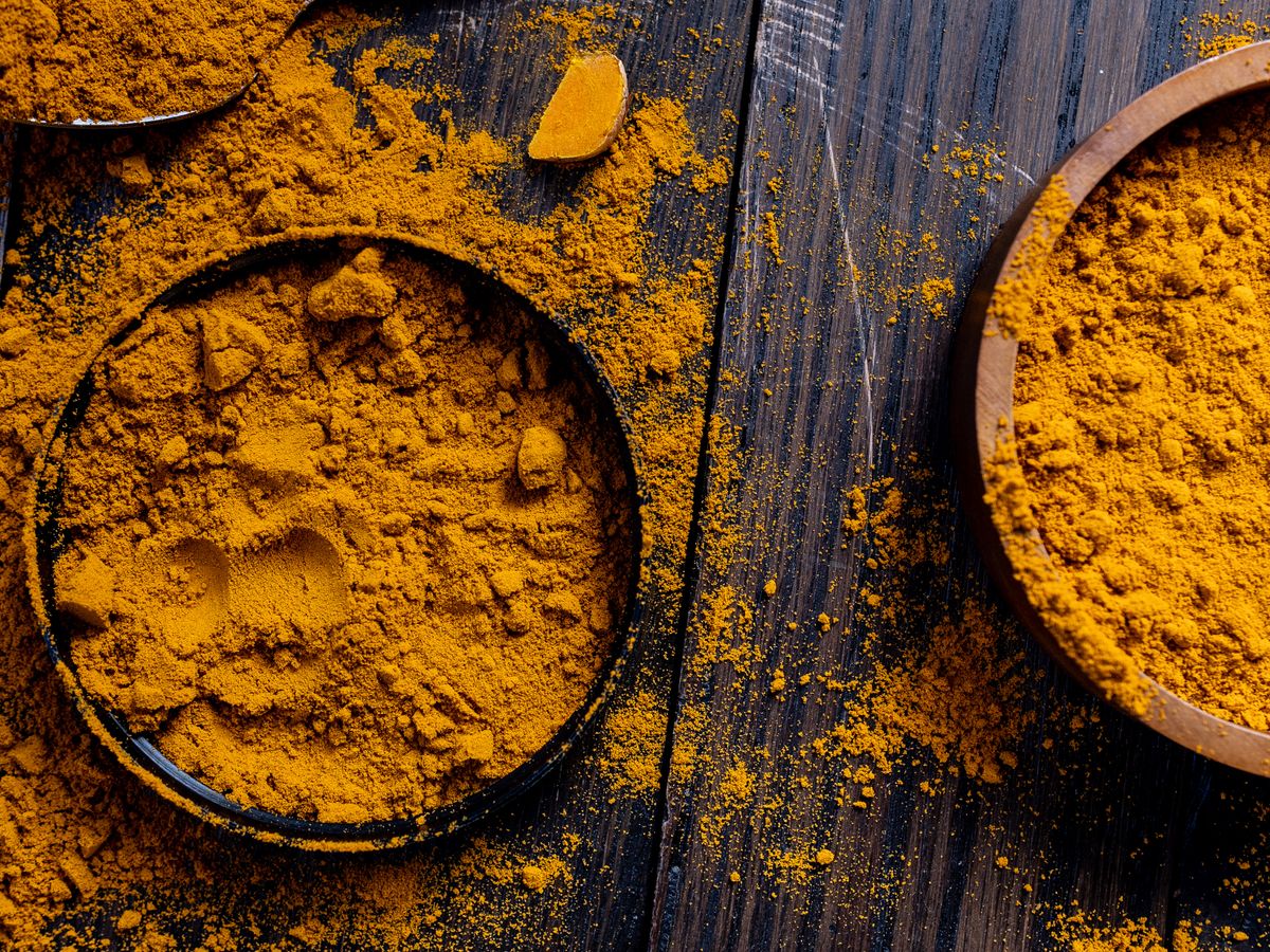 Bowls of bright golden turmeric powder on a dark wooden surface