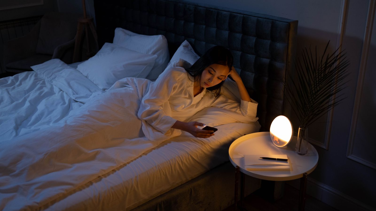 A woman lying awake in bed at night, lit by a soft bedside lamp