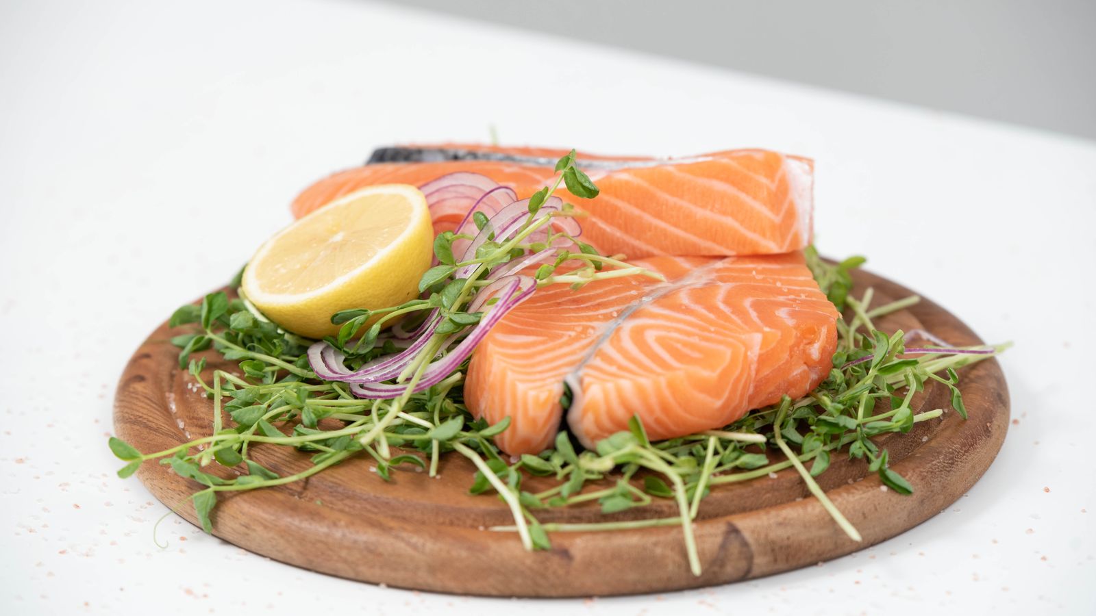 Fresh raw salmon fillets on a wooden board with lemon and microgreens