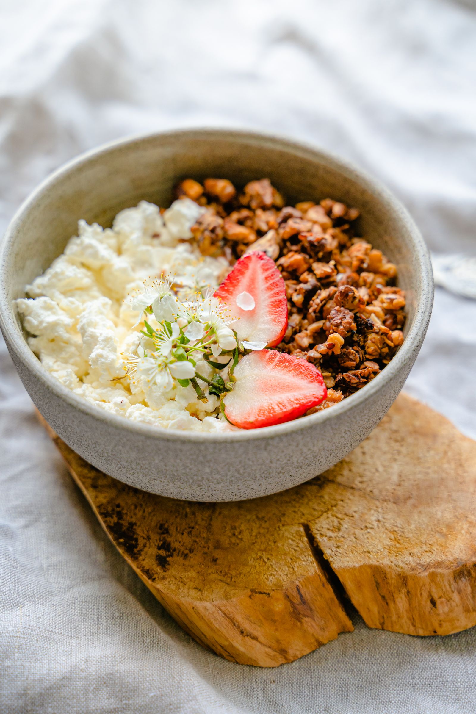 A bowl of cottage cheese with granola and strawberries on a wooden board