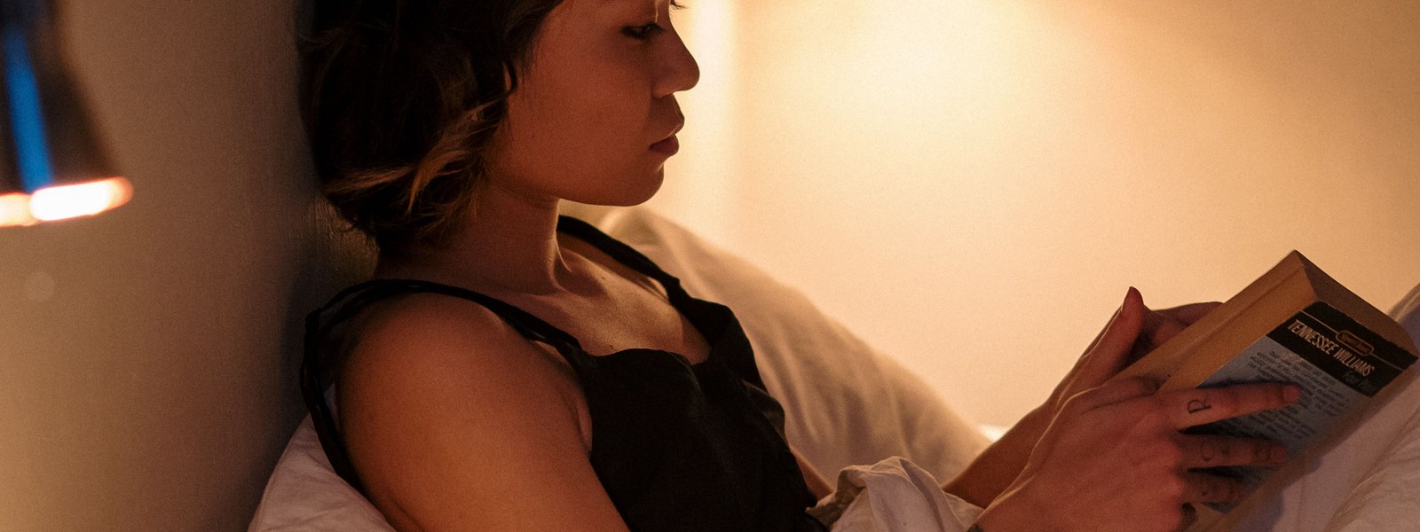 A person reading in bed by warm lamplight during an evening wind down