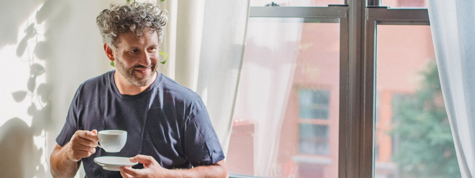 A man holding a cup of coffee in morning light by a window