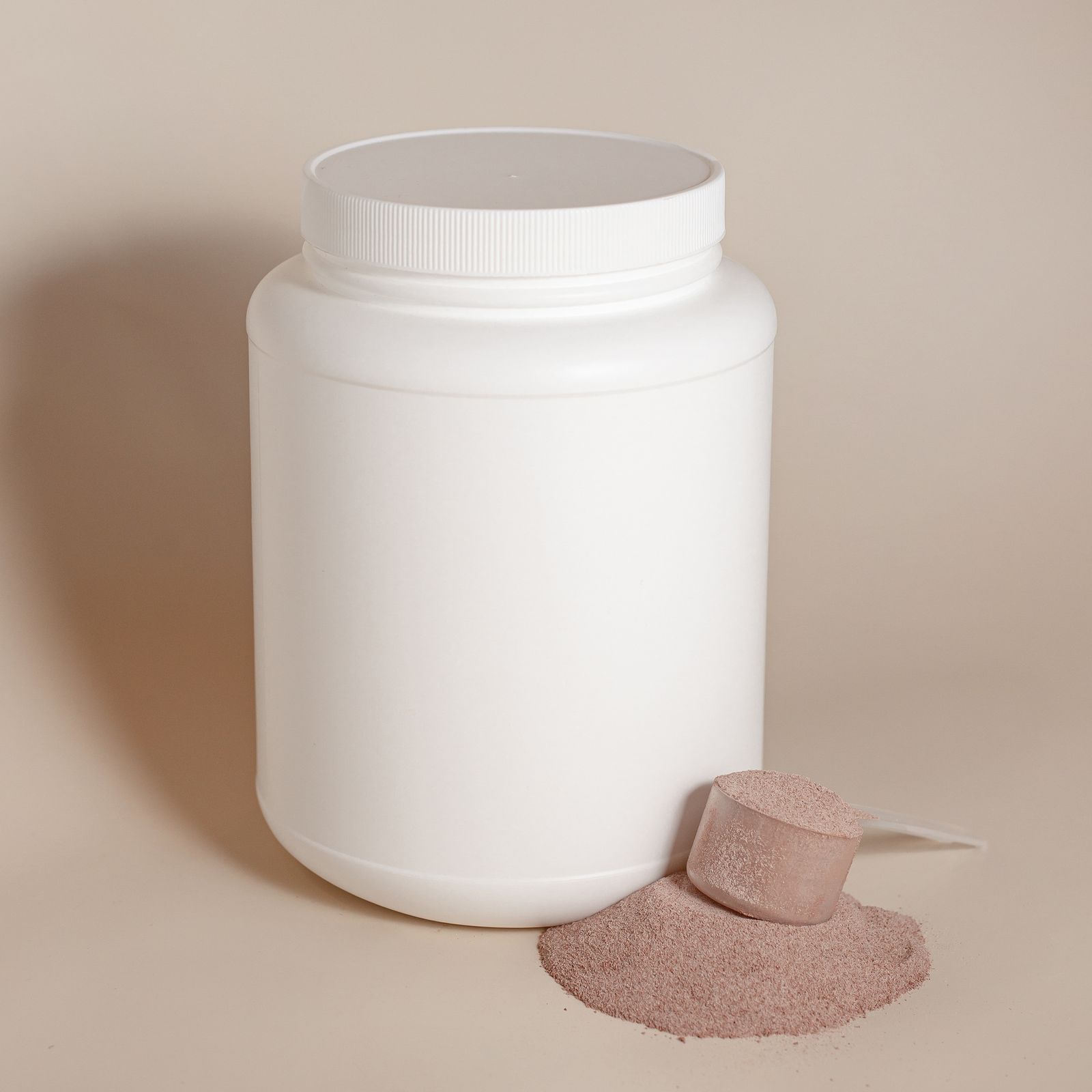 An unlabelled white protein tub beside a scoop and a small pile of powder
