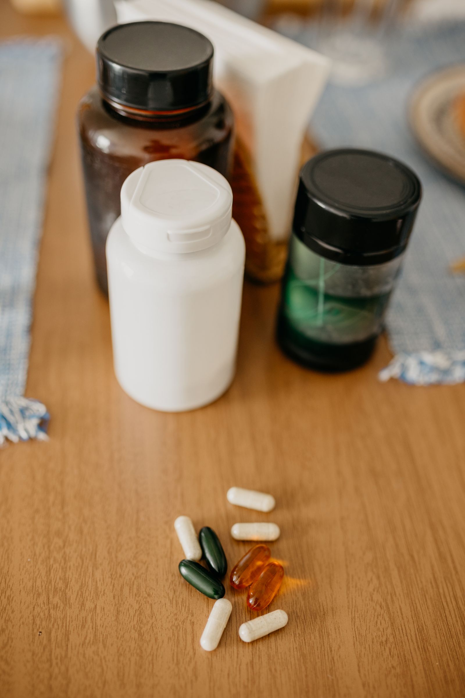 Three unlabelled supplement bottles on a wooden table with loose capsules in front of them