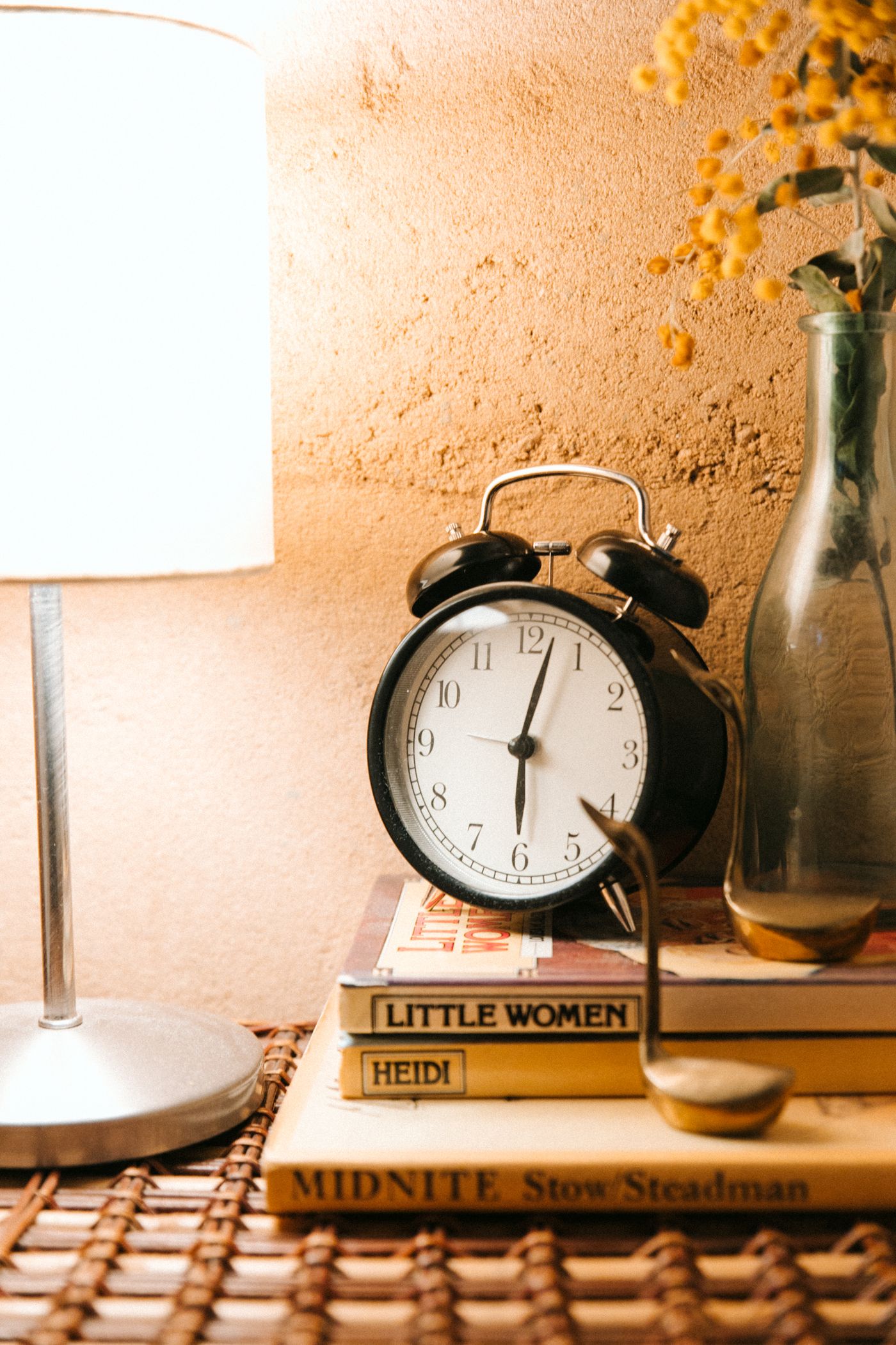 A black twin bell alarm clock on a stack of books beside a bedside lamp