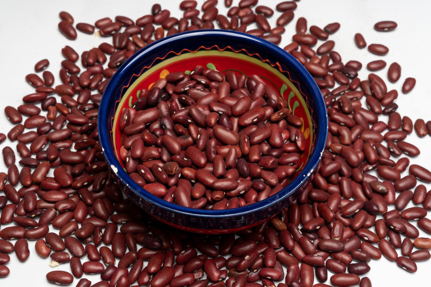 A blue ceramic bowl filled with dried red kidney beans, with more beans scattered around it