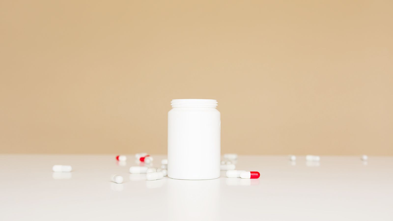 A plain white supplement bottle with capsules scattered around it on a warm neutral surface