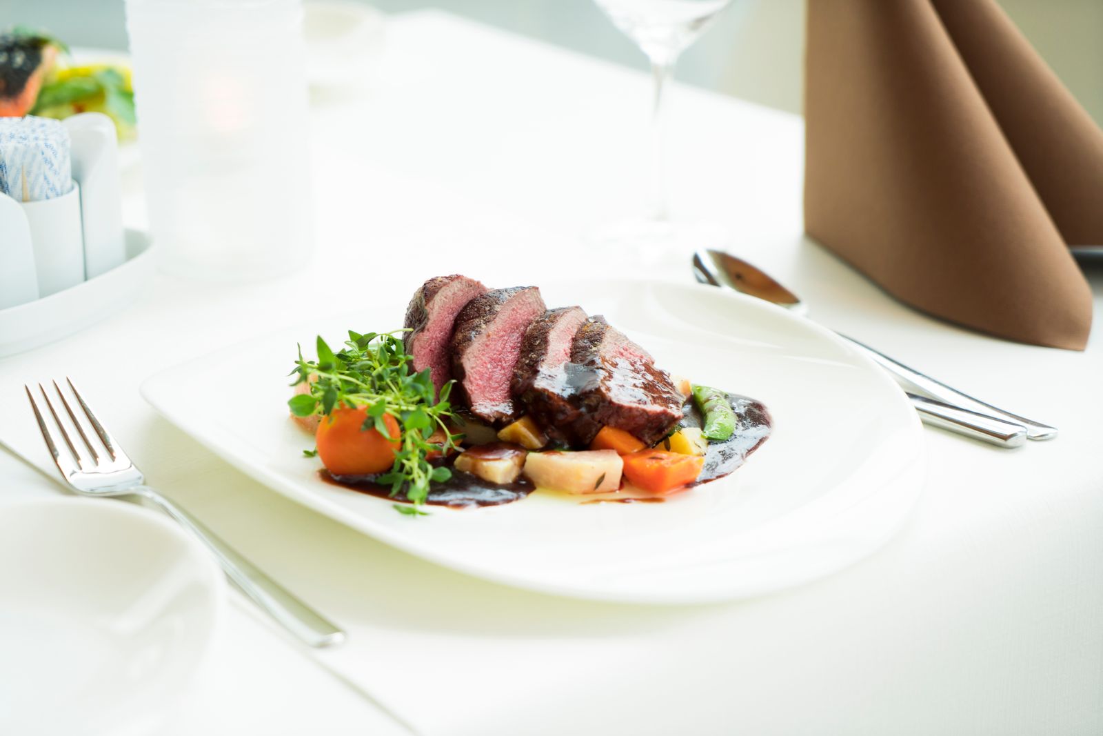 Sliced steak served with vegetables on a white plate at a set table