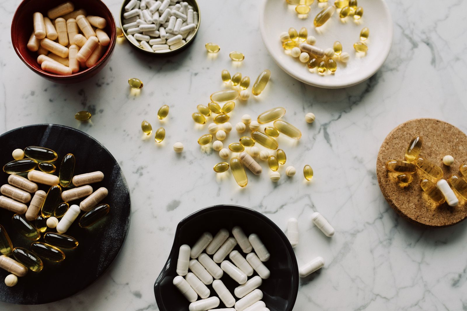 Capsules and softgels in small bowls on a marble surface