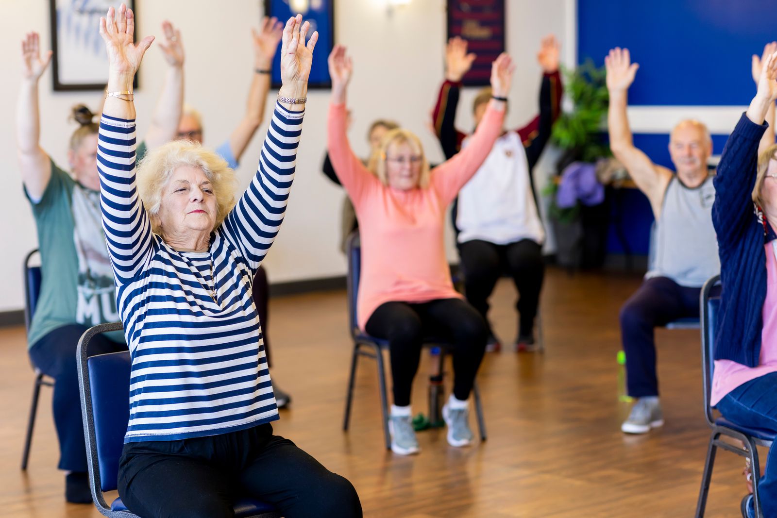 Older adults in a seated exercise class raising both arms overhead