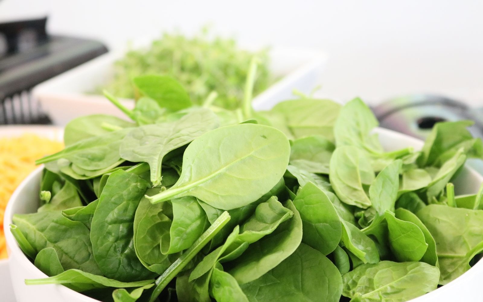 A white bowl heaped with fresh baby spinach leaves on a kitchen counter