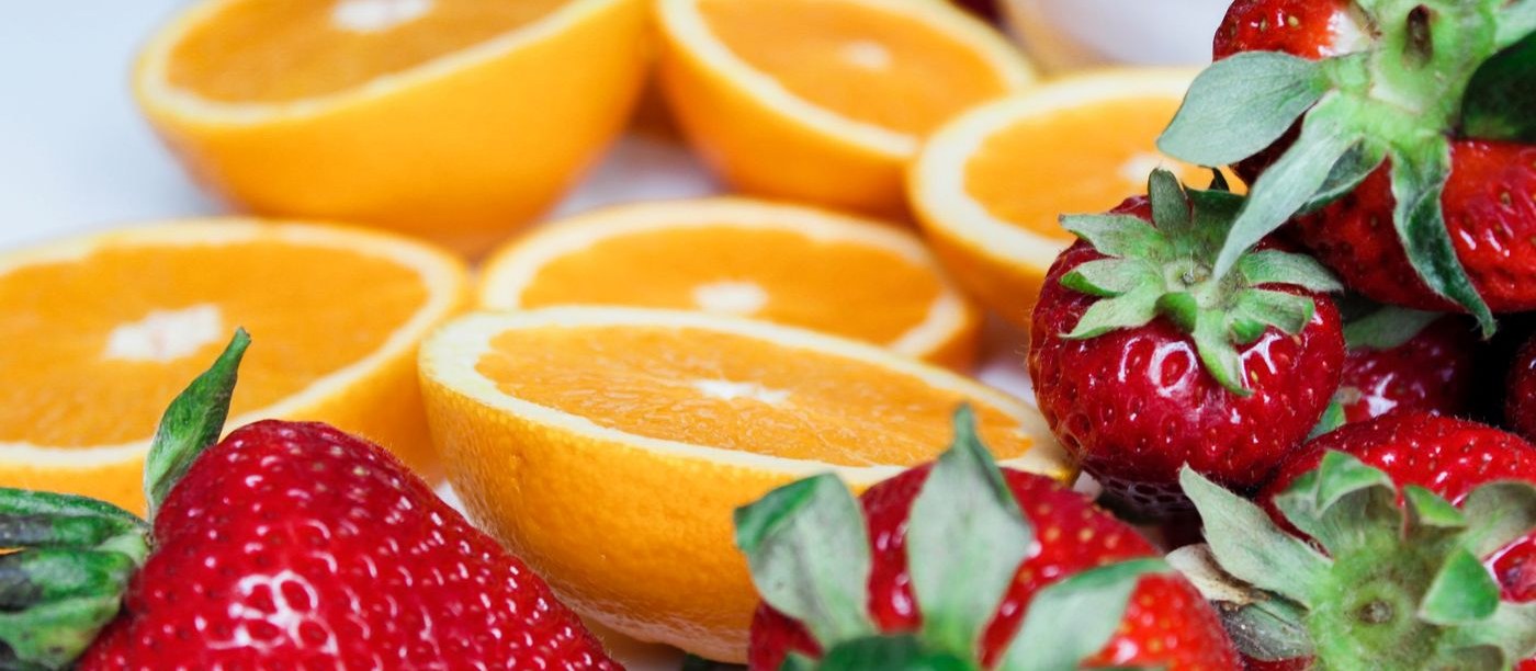 Halved oranges with fresh strawberries and berries on a white surface