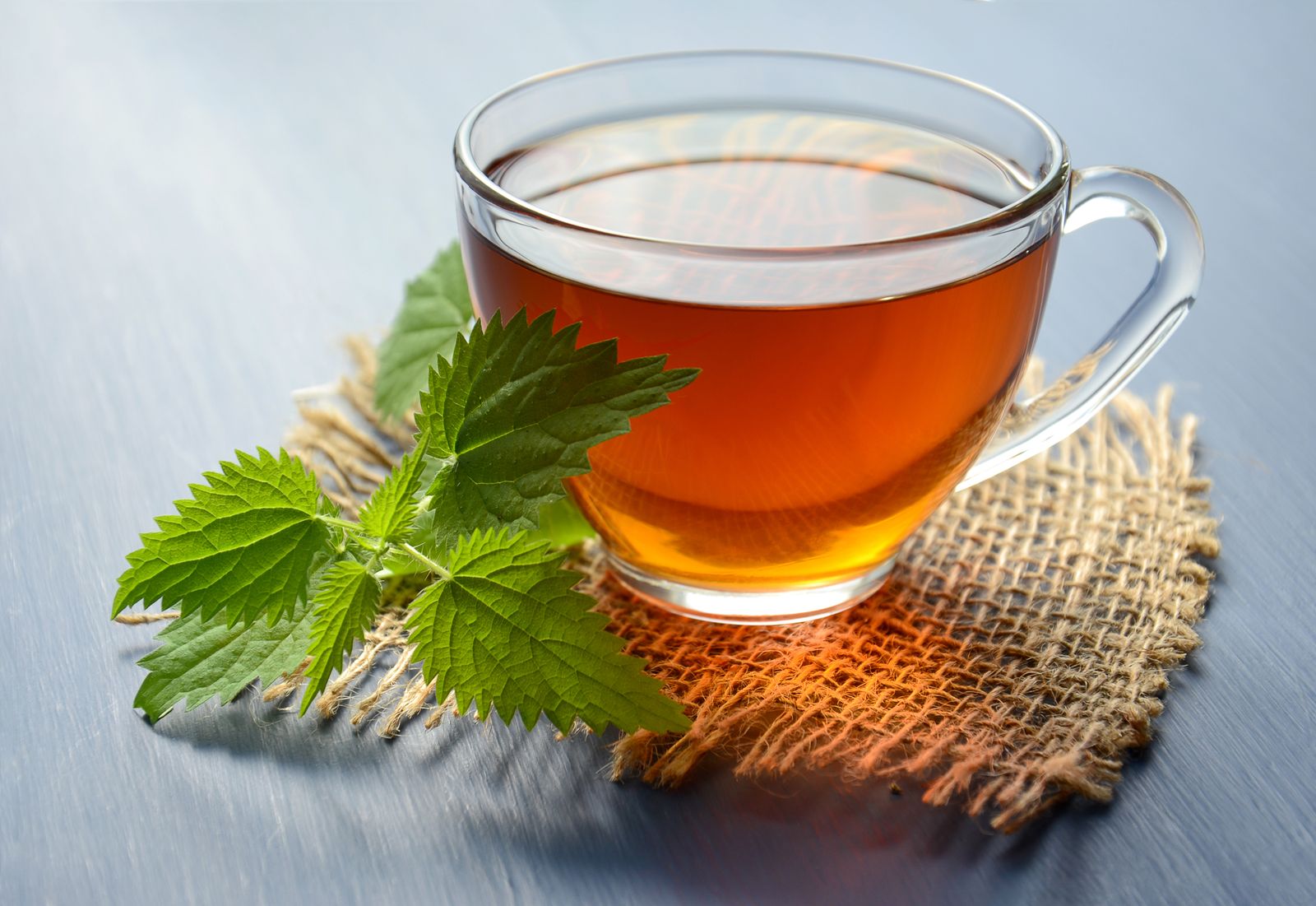 A clear glass cup of freshly brewed tea beside green leaves on a burlap mat