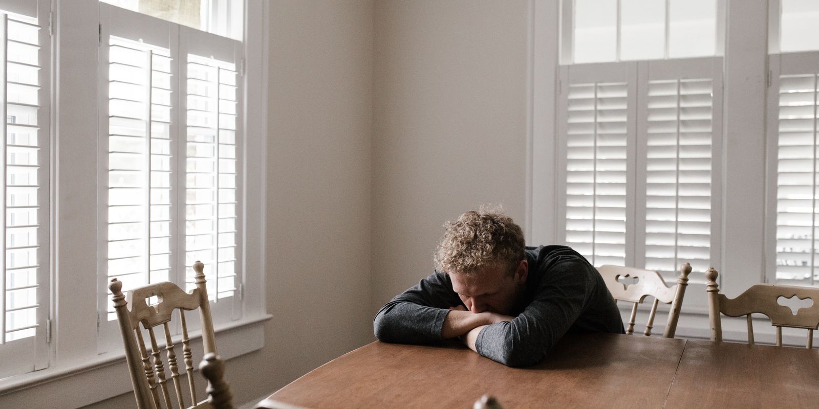 A man sitting alone at a table with his head down on his arms