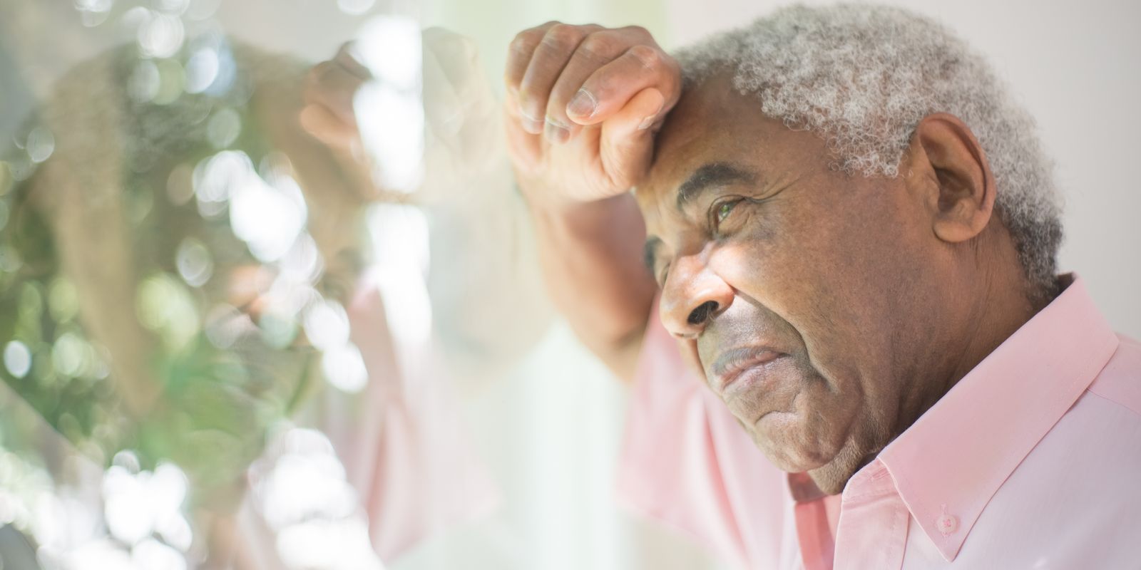 Senior man leaning against a window with his fist pressed to his forehead