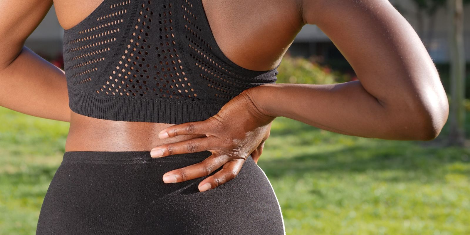 A woman in athletic wear holding her lower back outdoors in pain