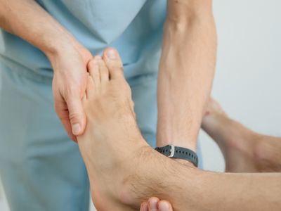 A clinician examining a patient's bare foot and big toe