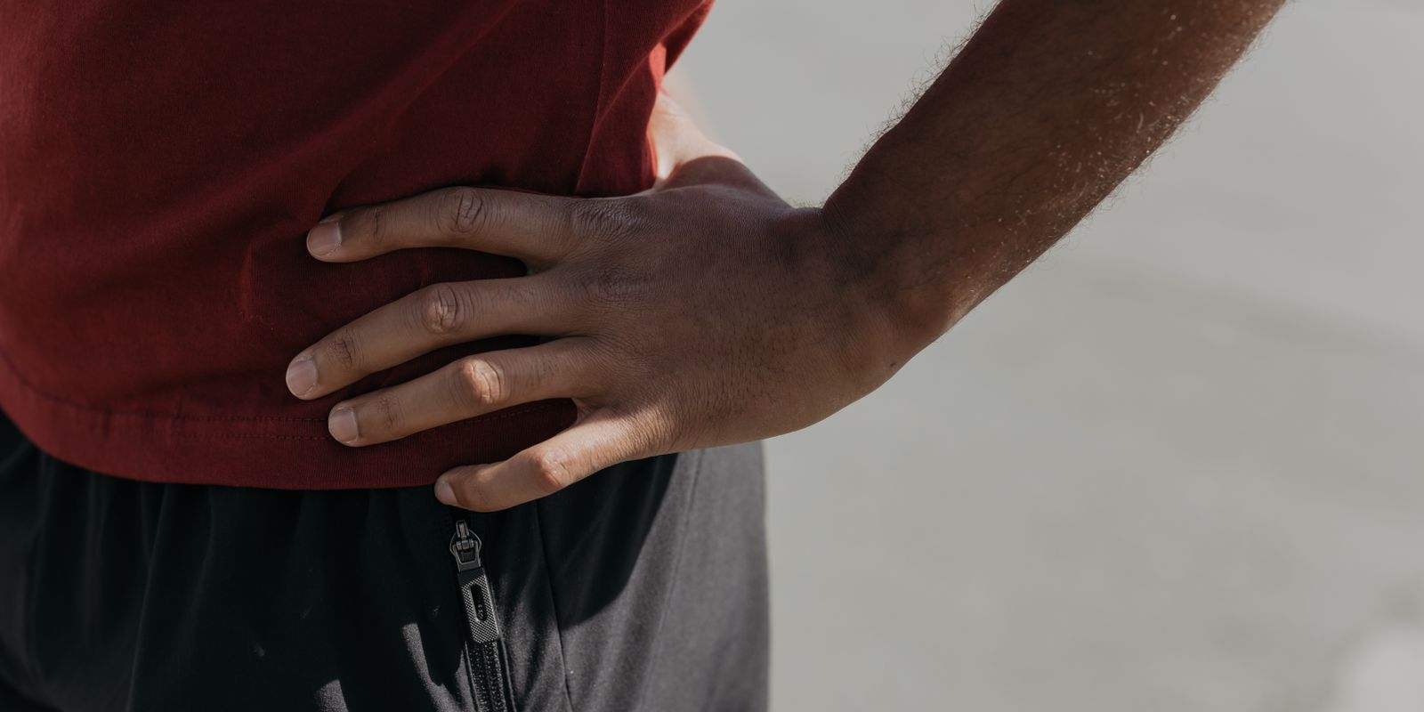A person in a red shirt pressing a hand into their side just above the waist