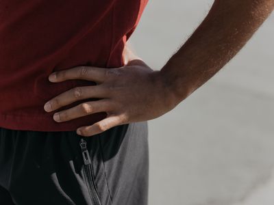 A person in a red shirt pressing a hand into their side just above the waist