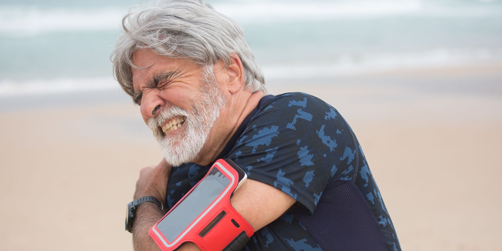 An older man grimacing and holding his shoulder with the opposite hand