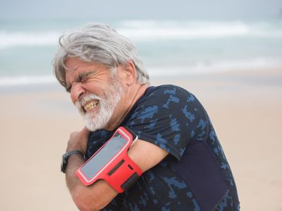 An older man grimacing and holding his shoulder with the opposite hand
