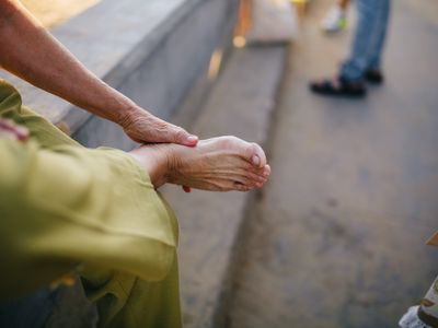 An older person in a green sleeve cradling their own bare foot while seated on a bench