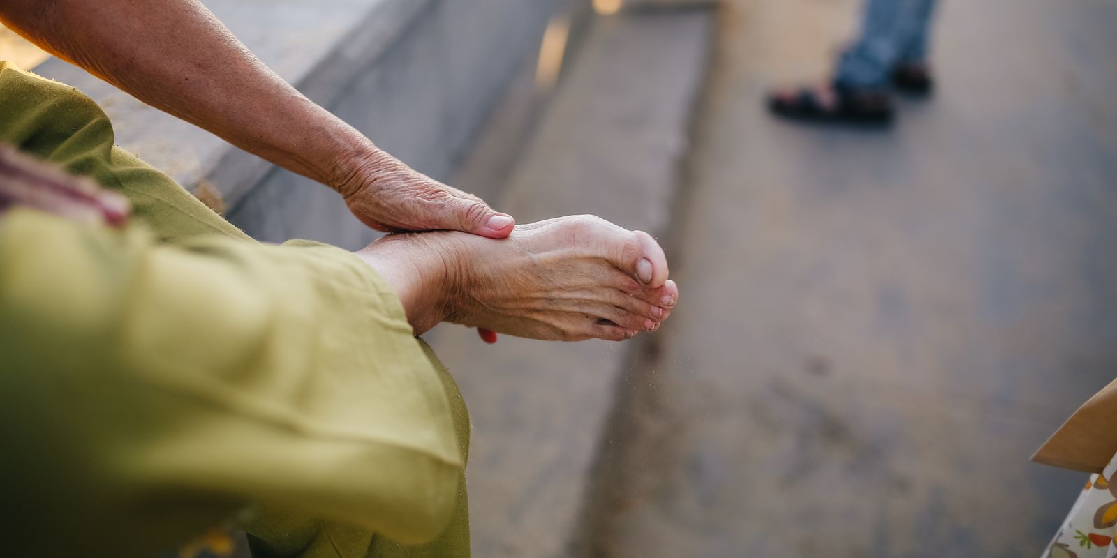 An older person in a green sleeve cradling their own bare foot while seated on a bench