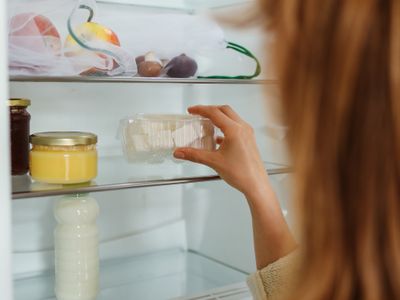A person placing a clear food container onto a lit refrigerator shelf