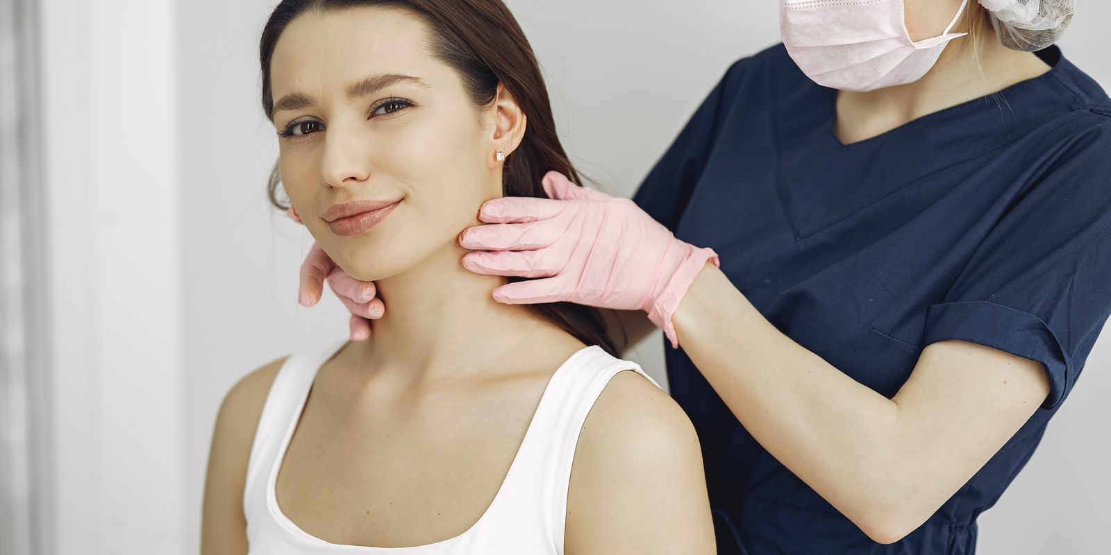 A clinician wearing gloves examining a woman's neck during a thyroid check