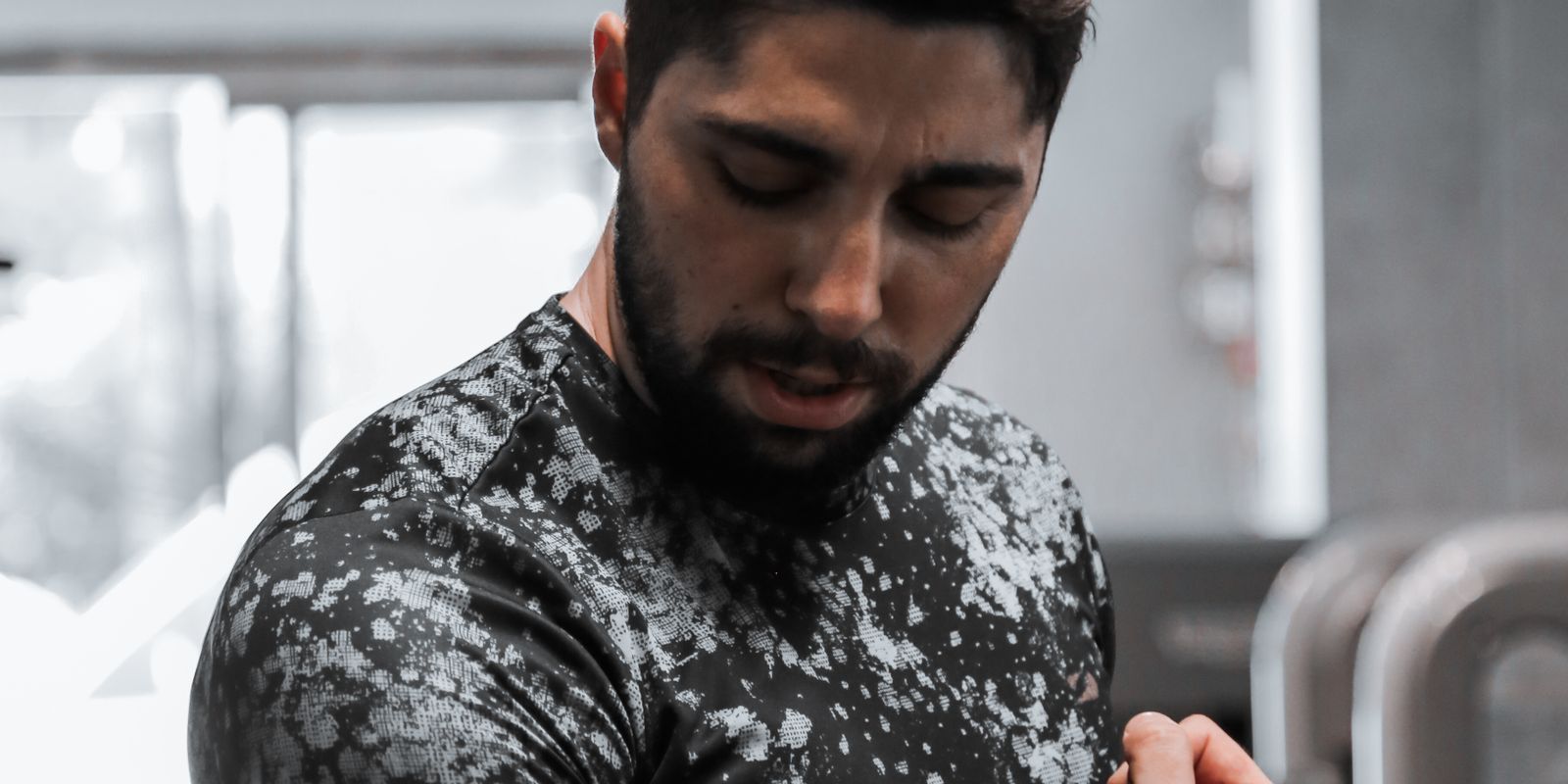 A man in a patterned shirt sitting in a gym with his head down catching his breath