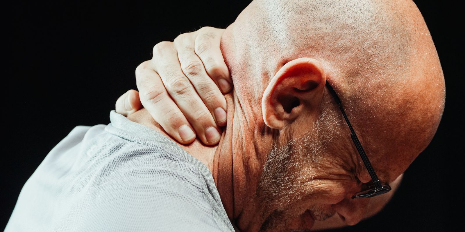 An older man in glasses wincing and gripping the back of his neck
