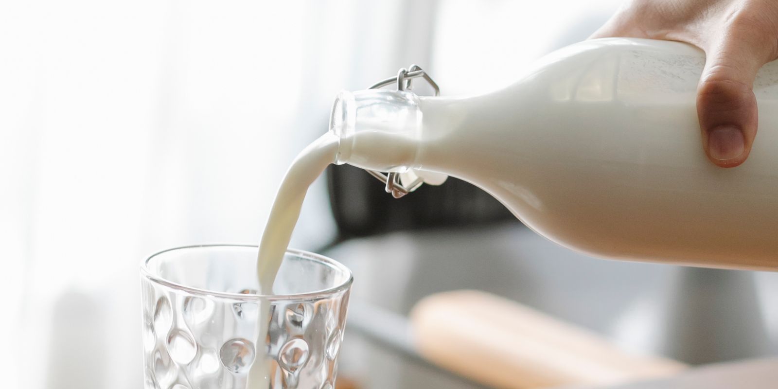 Milk poured from a glass bottle into a drinking glass on a bright counter