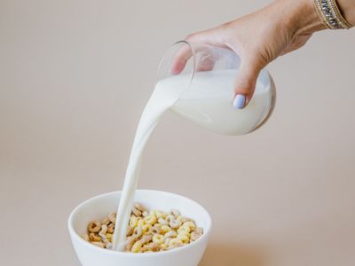 Milk poured from a small jug over a bowl of cereal and nuts