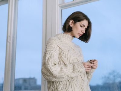A woman in a cream sweater standing by a bright window in winter