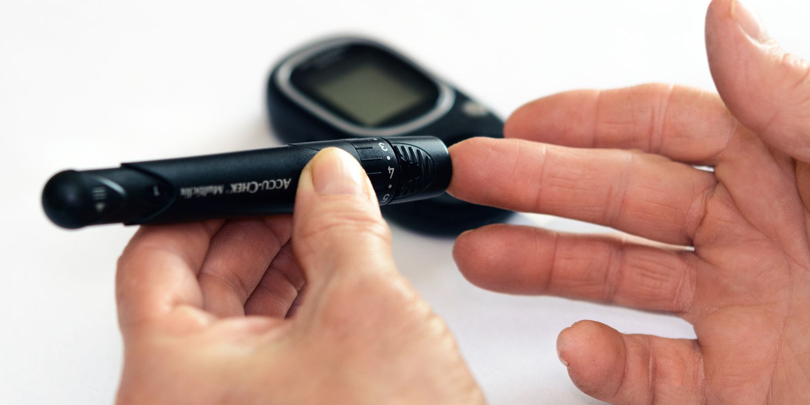 A person holding a lancet device against a fingertip beside a blood glucose meter