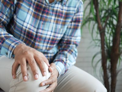 An older man in a plaid shirt sitting with his hand resting on his knee