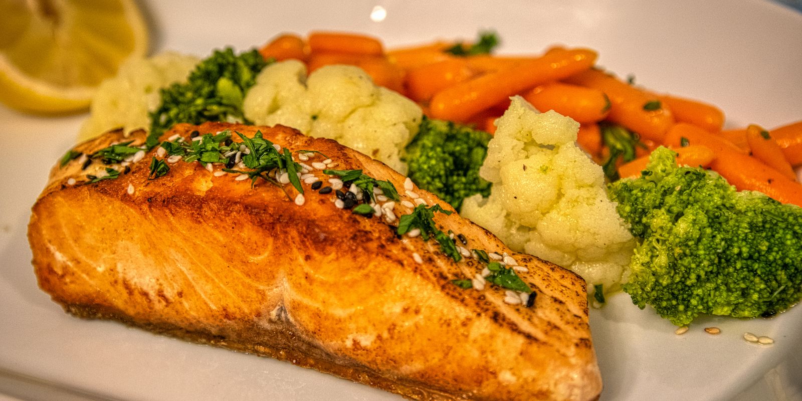 A cooked salmon fillet on a plate with broccoli, cauliflower and carrots