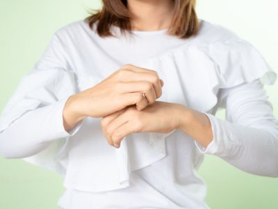 A person in a white top scratching the back of their forearm